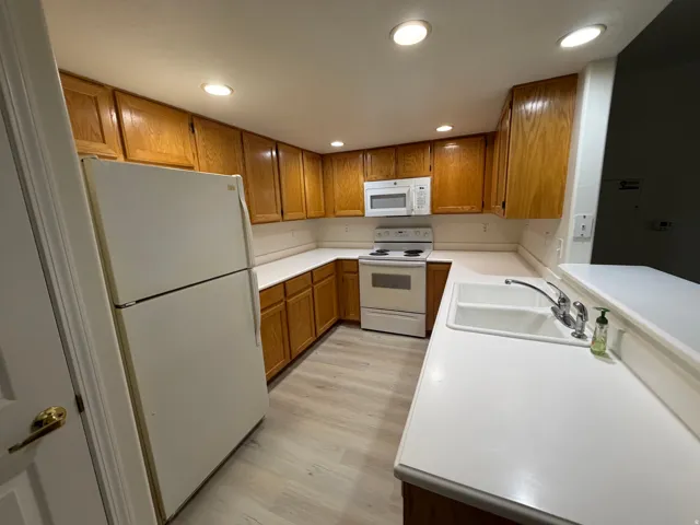 Kitchen featuring wood-finish cabinetry, white countertops, a double basin sink, and wood-finish flooring