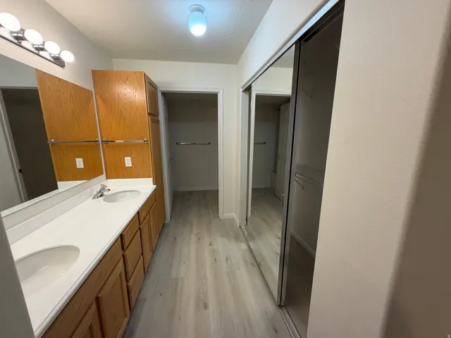 Dual sink vanity with white countertops, wood-finish cabinetry, and mirrored closet doors