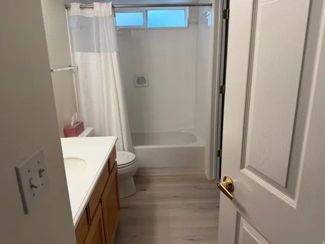 White vanity with an integrated sink, wood-finish cabinetry, and light wood-finish flooring