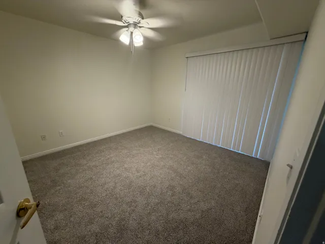 Plush gray carpeting, vertical blinds, ceiling fan with integrated lighting, and white trim