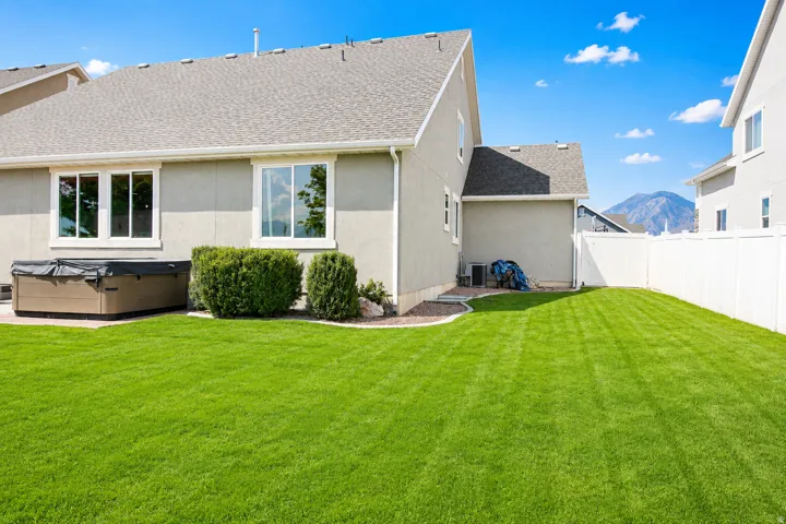 Expansive backyard featuring a manicured lawn, established landscaping, privacy fencing, and a built-in spa