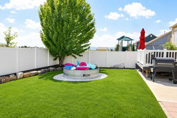 Expansive green lawn, white privacy fencing, mature tree, white gravel accent area, and a wood deck