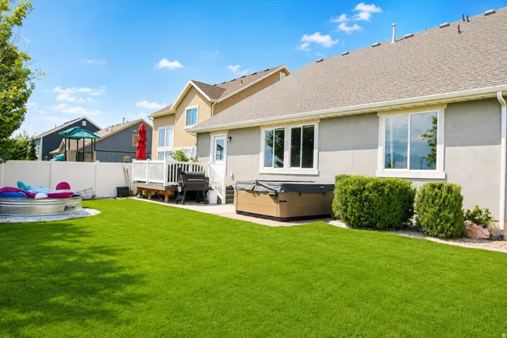 Expansive green lawn with a white privacy fence, multi-level composite deck, and built-in hot tub