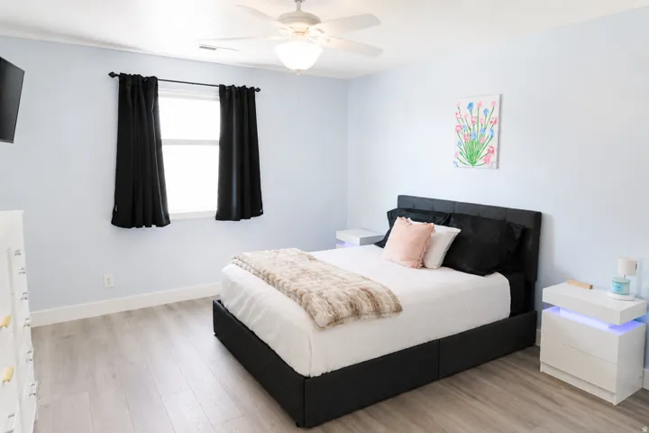 Recessed lighting with a ceiling fan, light blue wall paint, window with black curtains, and wood-finish flooring