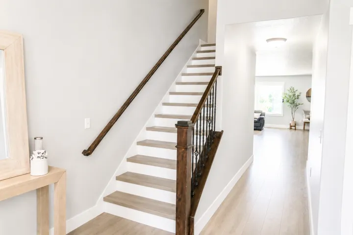 Staircase with wood-finish treads and risers, dark wood handrail, and wrought iron balusters