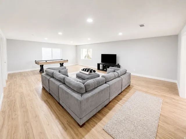 Expansive open-concept room featuring wood-finish flooring, recessed lighting, and multiple windows with plantation shutters