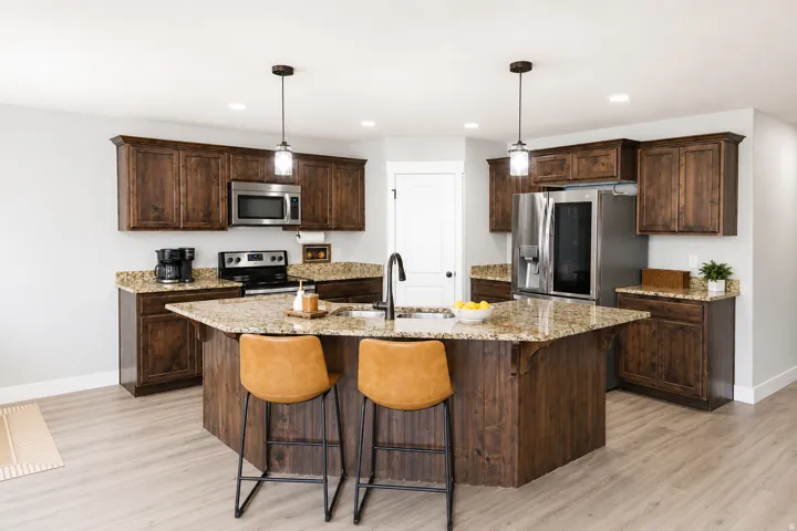 Kitchen featuring wood-finish cabinetry, light-toned wood-finish flooring, stainless steel appliances, pendant lighting, and a kitchen island with stone countertops