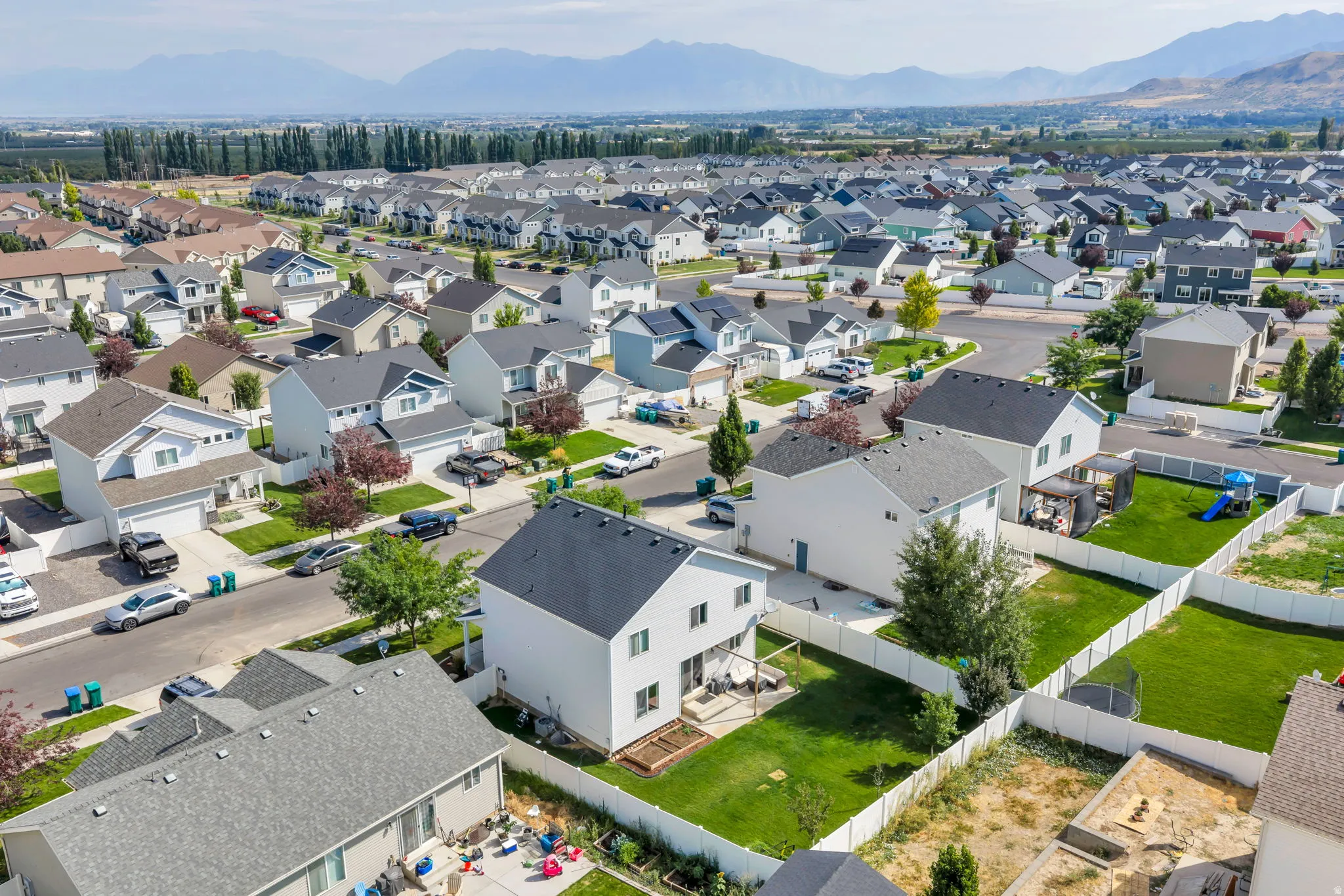 Expansive neighborhood with a consistent architectural style, featuring individual homes with attached garages, manicured lawns, and mountain scenery in the background