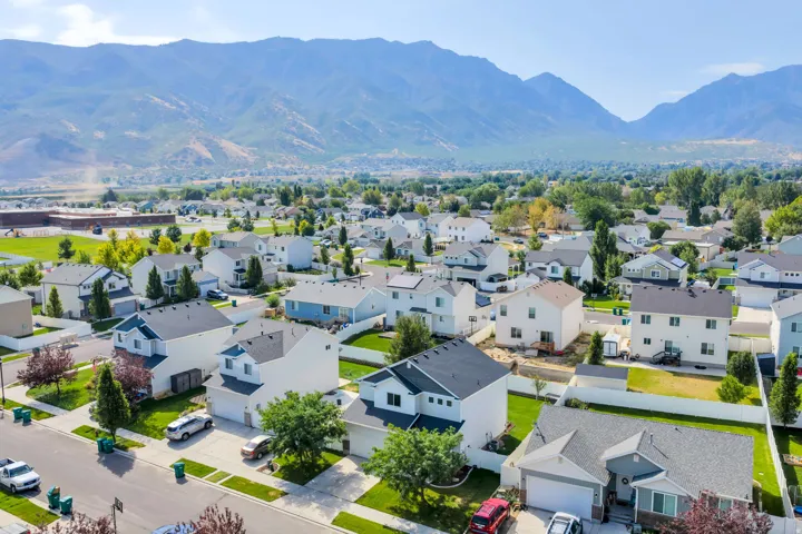 Aerial view of a residential community nestled against mountain backdrop, featuring single-family homes with modern architectural styling, manicured lawns, mature landscaping, and attached garages