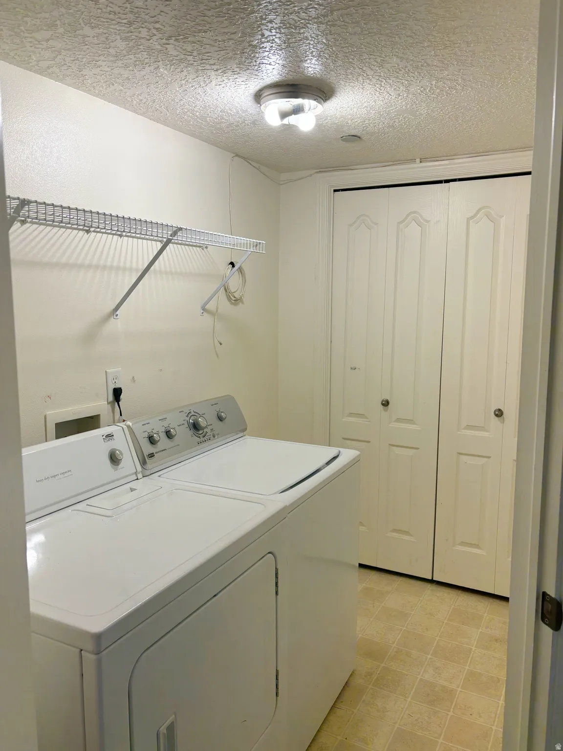 Laundry area with wire shelving, bi-fold closet doors, and light-toned flooring