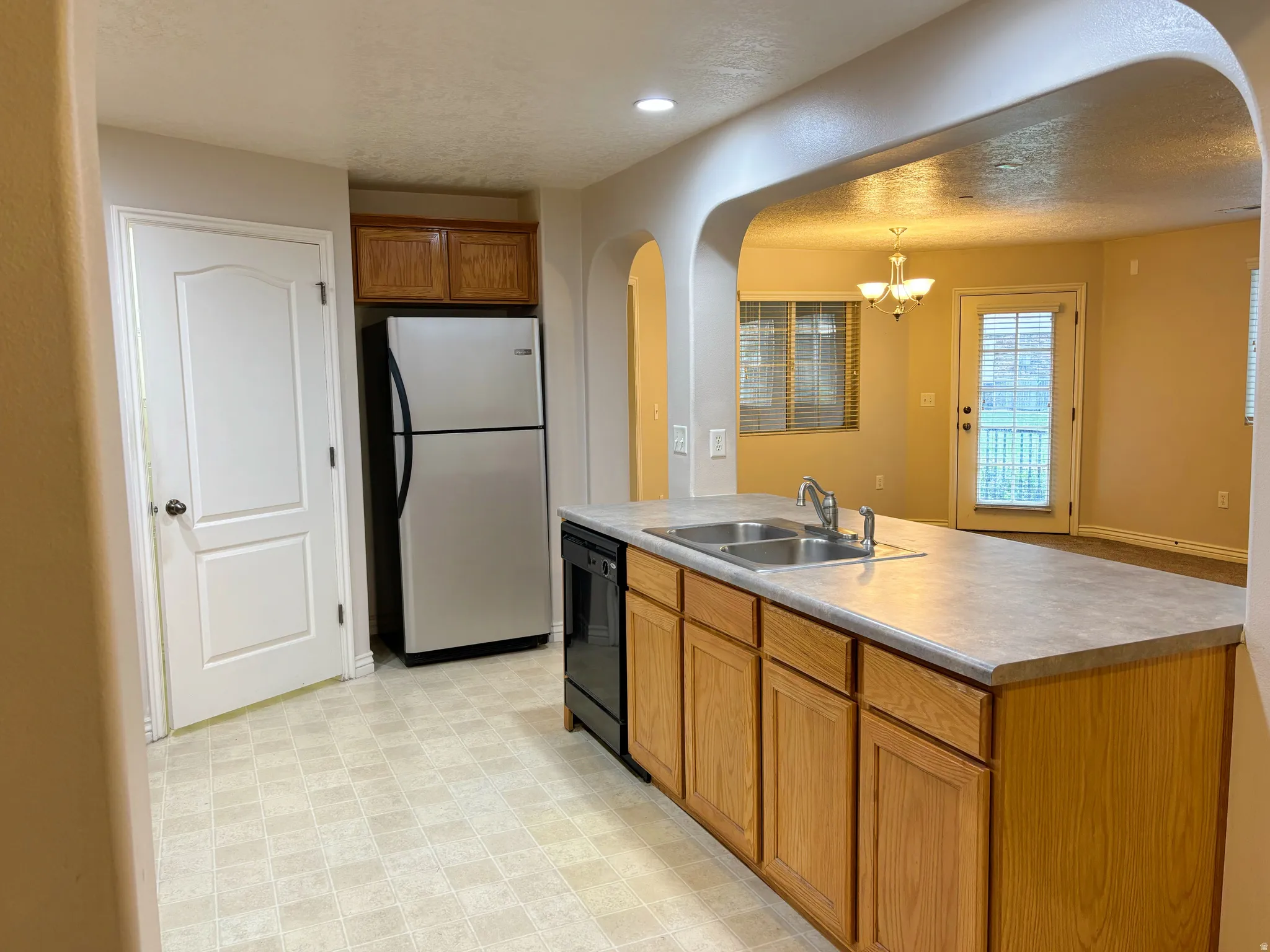 Kitchen featuring a double basin sink, built-in dishwasher, wood-finish cabinetry, and a stainless steel refrigerator