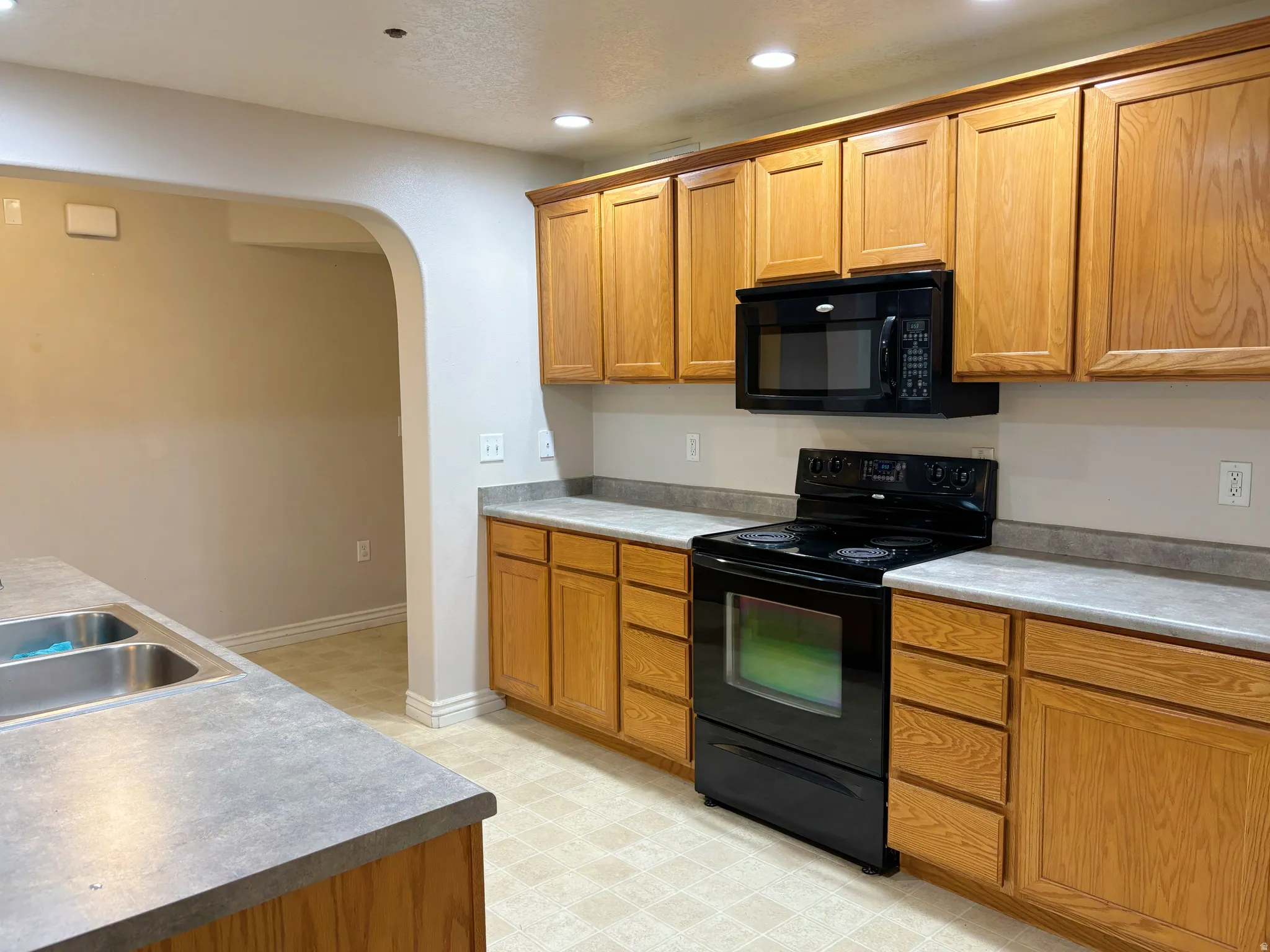 Kitchen featuring wood cabinetry, laminate countertops, a double basin stainless steel sink, and black appliances including a range and microwave
