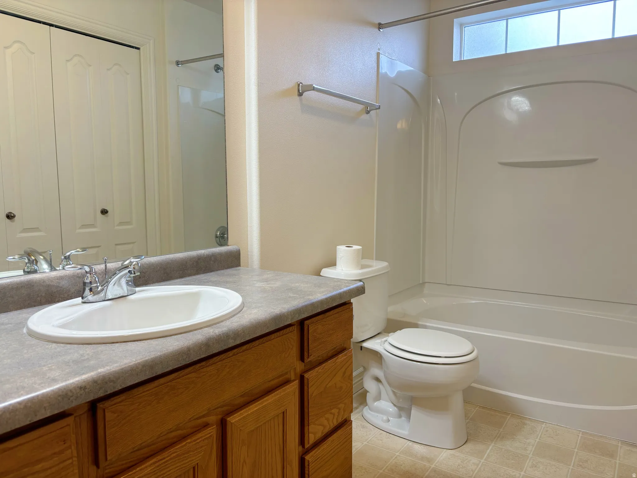 Bathroom featuring a wood-finish vanity with an oval sink, a light-toned countertop, a shower-over-tub combination, and tiled flooring