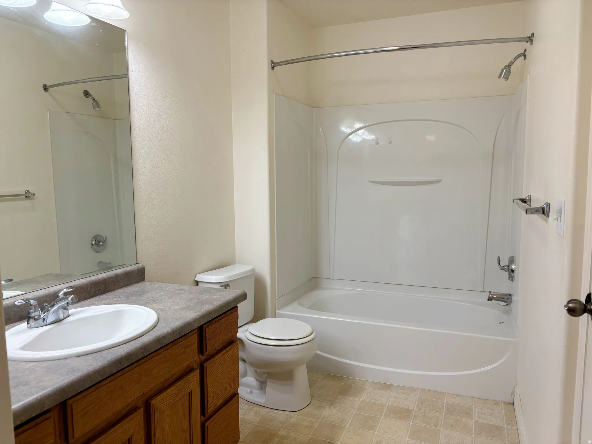 Spacious bathroom featuring a wood-finish vanity with dual-sink configuration and stone countertop, combined tub and shower with curved enclosure and glass door, and ceramic tile flooring throughout