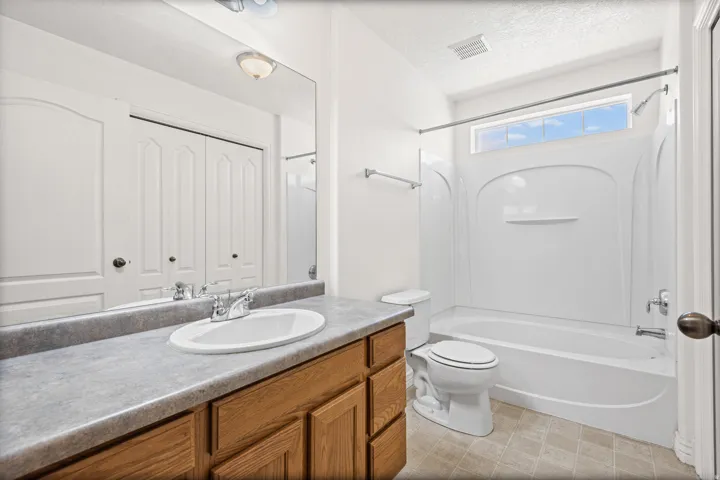 Vanity with wood cabinetry and countertop, integrated sink with chrome faucet, large wall mirror, and a full bathtub with overhead shower