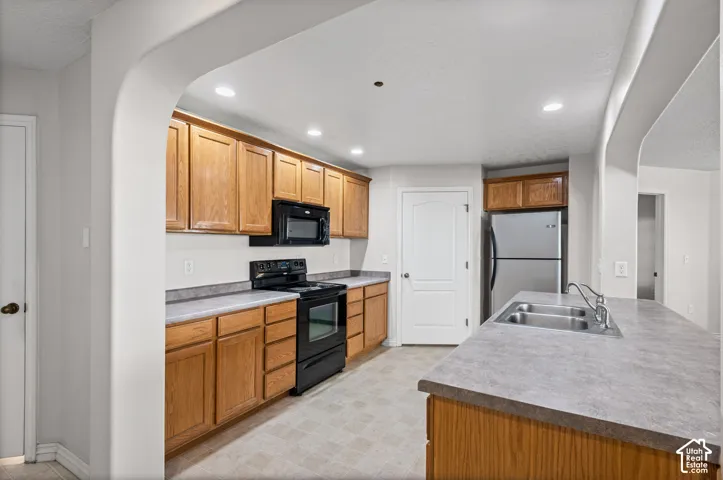 Kitchen featuring wood cabinetry, stainless-steel double sink, black appliances, and recessed lighting