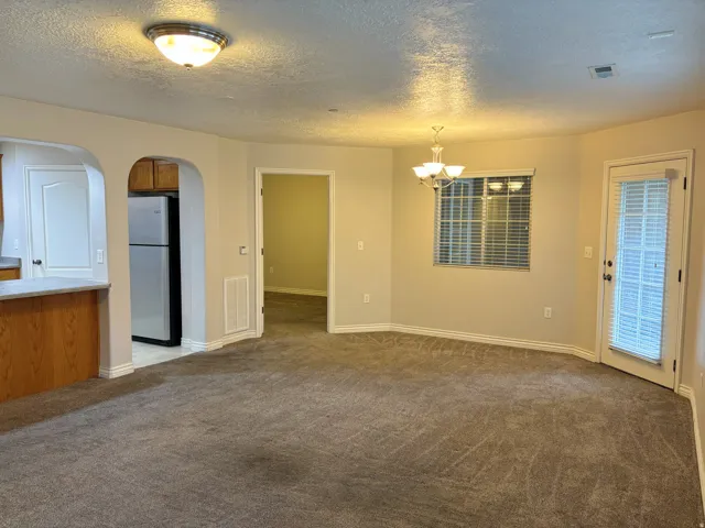Spacious living area featuring carpet flooring, an arched entryway, a built-in breakfast bar with wood-finish cabinetry, and a private exterior door