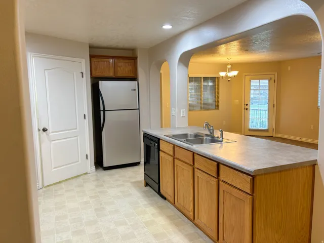 Kitchen featuring a double basin sink, built-in dishwasher, wood-finish cabinetry, and a stainless steel refrigerator
