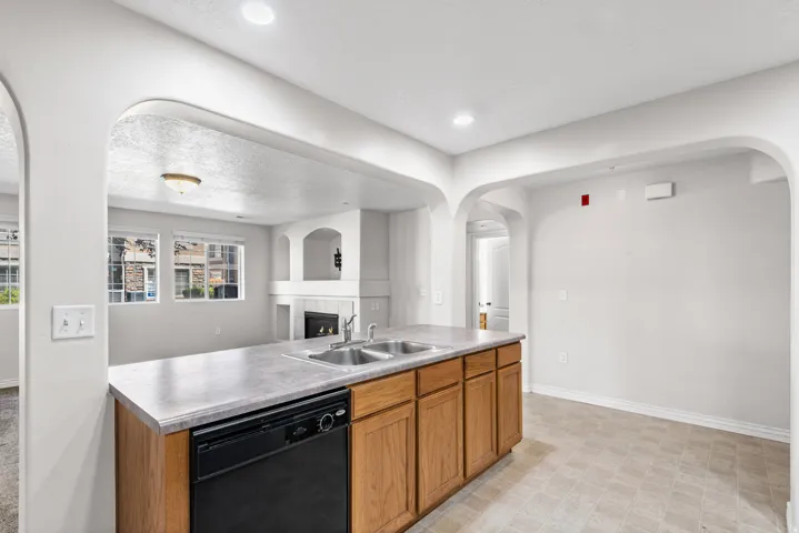 Kitchen island with integrated double basin sink, dark finish dishwasher, wood-finish cabinetry, and solid surface countertop