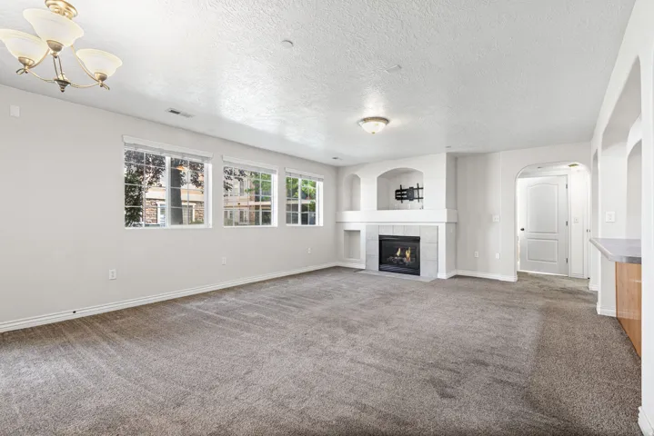 Spacious living area featuring a fireplace with a light-toned tile surround, built-in shelving, multiple windows, and neutral carpeting