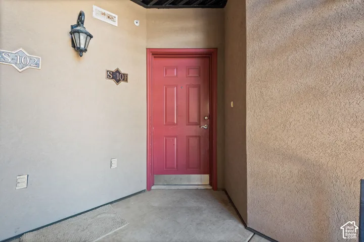 Red paneled entry door with silver-tone hardware, stucco exterior finish, and a wall-mounted lantern light fixture