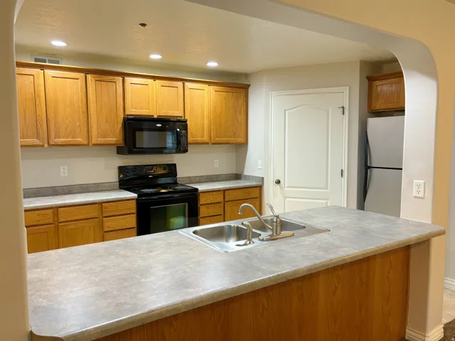Kitchen featuring wood-finish cabinetry, a stainless steel double basin sink, and black appliances