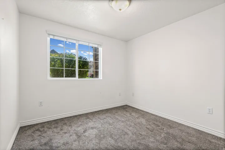 Interior room featuring white walls, textured carpeting, and a window with white grilles