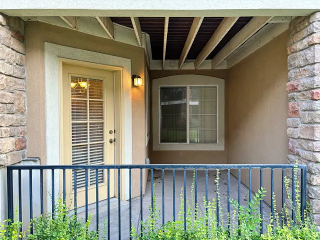 Covered outdoor patio featuring a stucco exterior, stone column, and a glass-paneled door