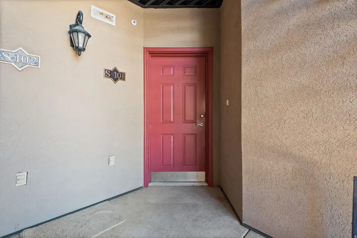 Red paneled entry door with silver-tone hardware, stucco exterior finish, and a wall-mounted lantern light fixture