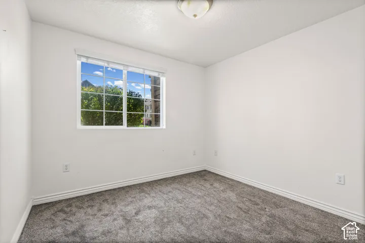Interior room featuring white walls, textured carpeting, and a window with white grilles