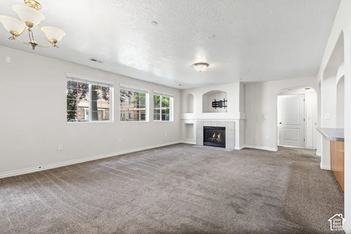 Spacious living area featuring a fireplace with a light-toned tile surround, built-in shelving, multiple windows, and neutral carpeting
