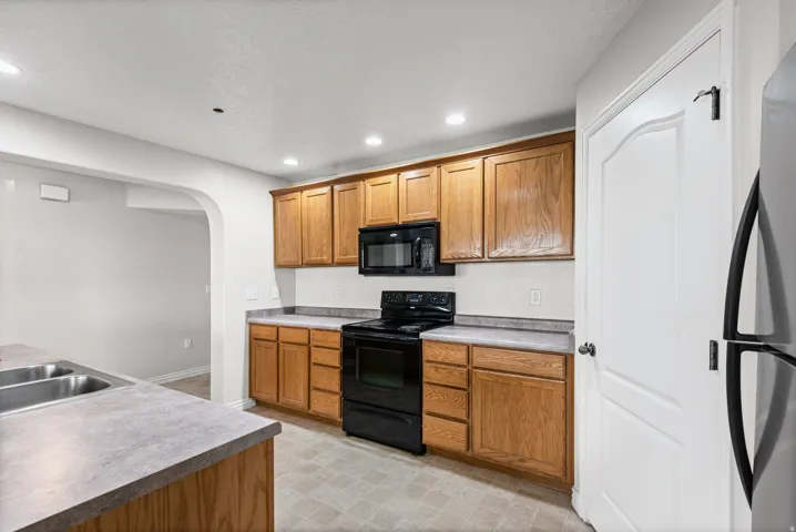 Kitchen featuring wood cabinetry, laminate countertops, black appliances, recessed lighting, and an arched doorway