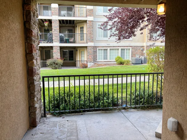 Concrete patio with an exterior wall light fixture, black metal railing, and a stone accent column