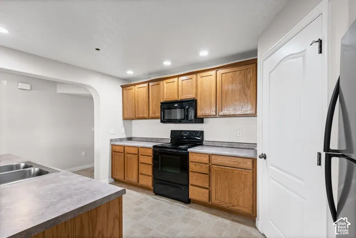 Kitchen featuring wood cabinetry, laminate countertops, black appliances, recessed lighting, and an arched doorway