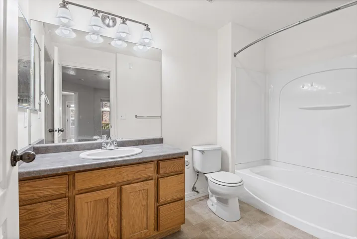 Bathroom featuring a wood-finish vanity with a single basin sink, an expansive mirror, a four-light fixture, and a tub with a shower surround