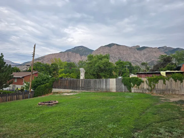 Expansive grassy yard featuring a brick fire pit and wood fencing