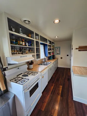 Expansive kitchen featuring wood-finish flooring, wood countertops, built-in shelving, a double basin sink, and recessed lighting