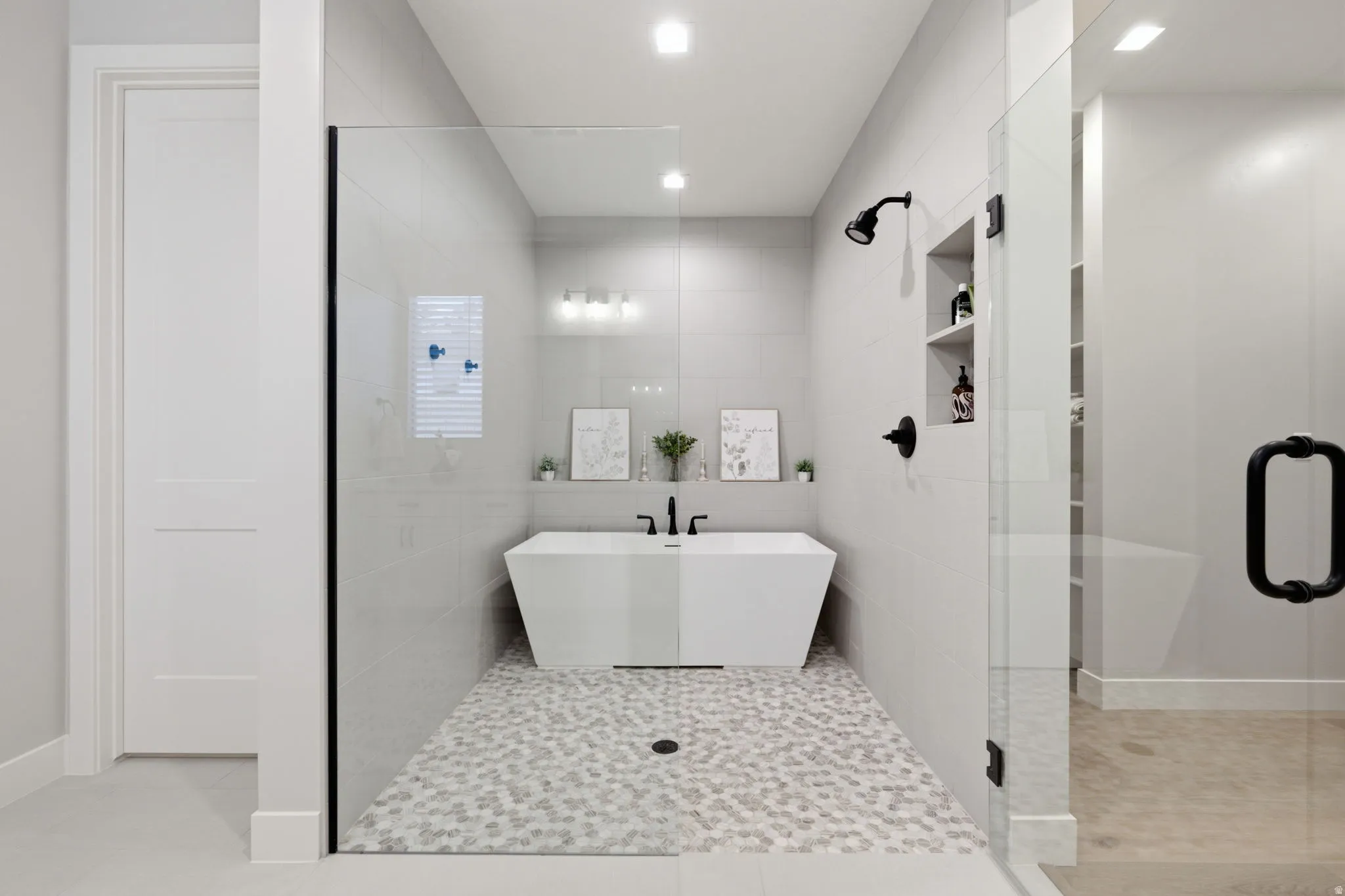 Walk-in shower with a glass enclosure, free standing tub, white hexagon tile flooring, and matte black fixtures
