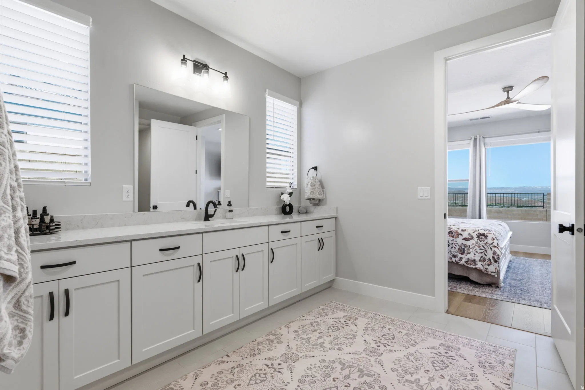 vanity with light gray cabinetry, matte black hardware, and an expansive quartz countertop