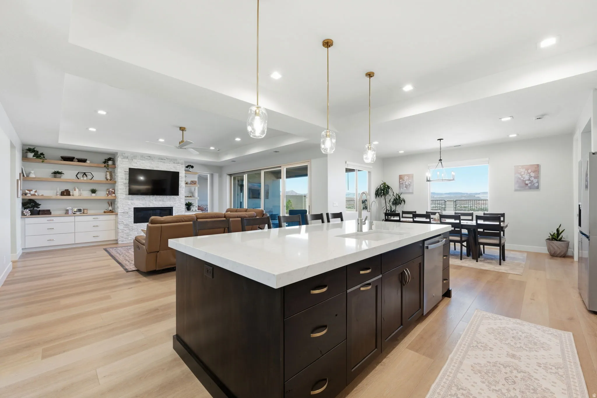 Open-concept living area featuring LVP wood-finish flooring, a contemporary kitchen island with a white countertop, and a fireplace with a textured stone surround
