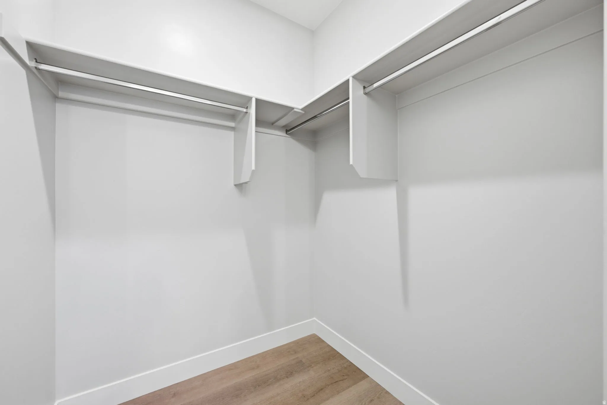 Walk-in closet featuring LVP wood-finish flooring, white walls, and built-in shelving with hanging rods