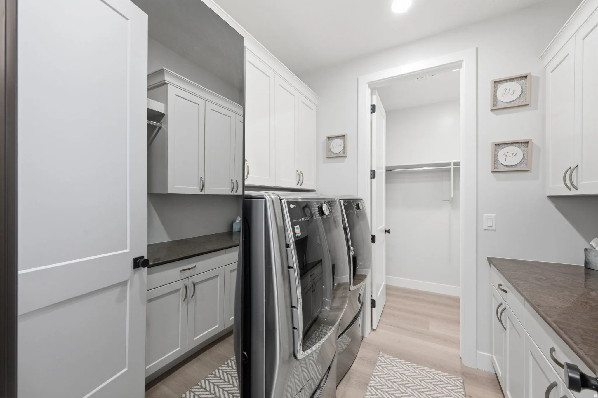 Laundry room featuring extensive white cabinetry, dark countertops, wood-finish flooring, and a built-in hanging rod