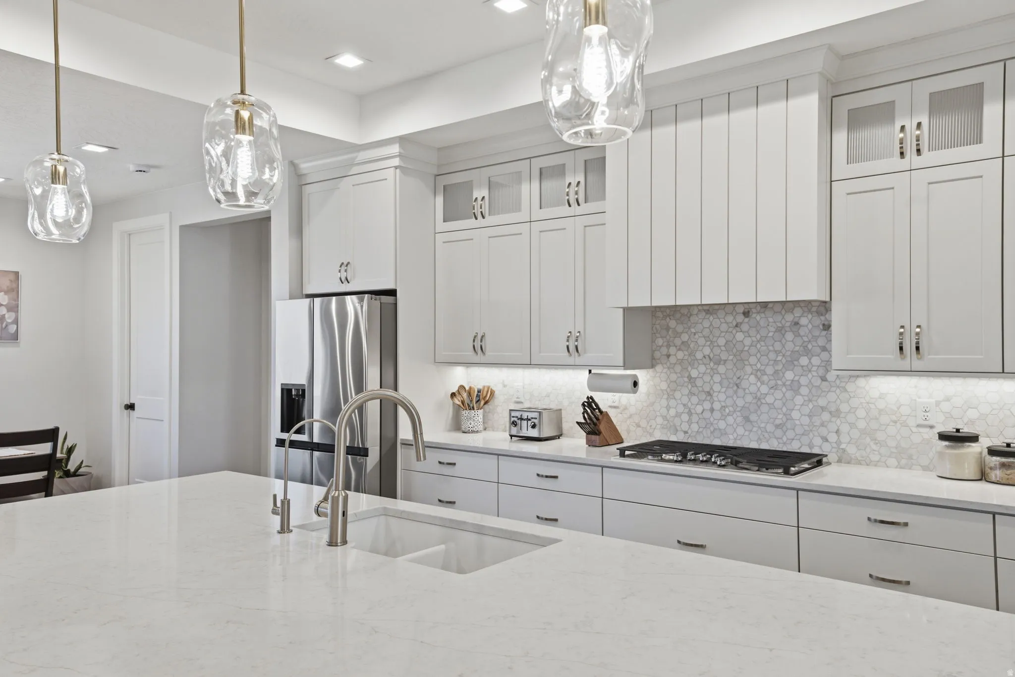 Kitchen featuring a large island with an undermount sink, stainless steel appliances, light-toned cabinetry, Range hood / vented out, honeycomb tile backsplash, and recessed lighting