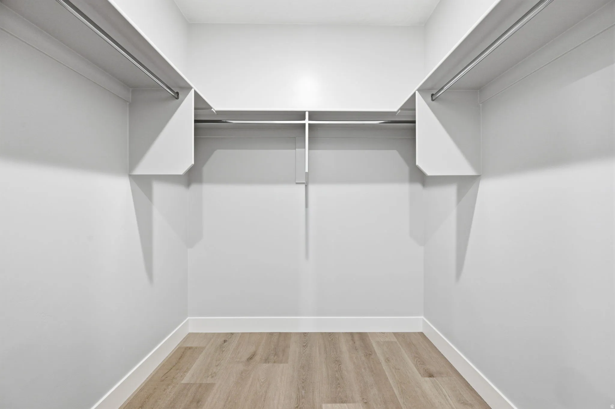 Walk-in closet featuring LVP wood-finish flooring, white walls, and built-in shelving with hanging rods