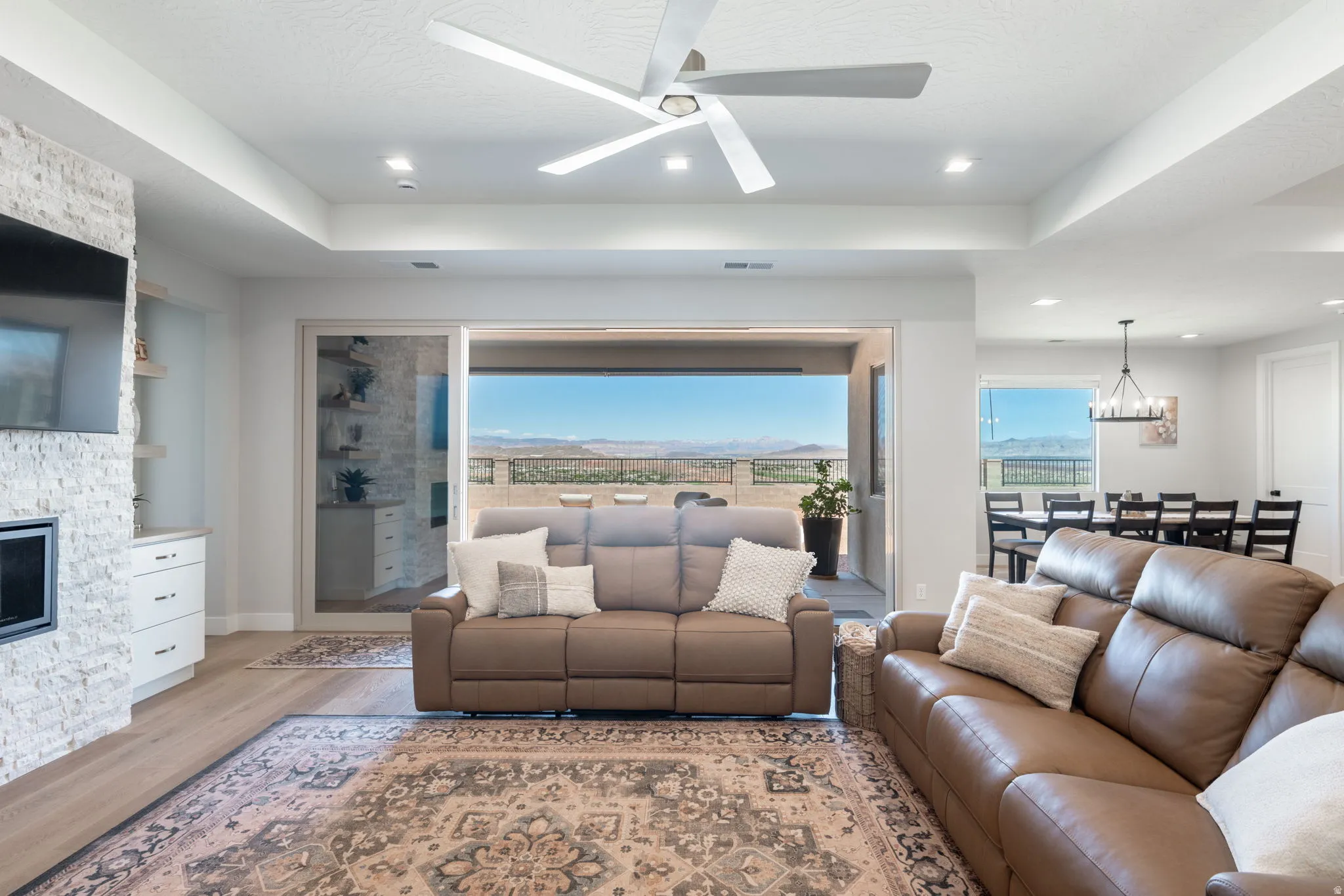 Living area with wood-finish flooring, a stacked stone fireplace with built-in cabinetry, and a modern ceiling fan