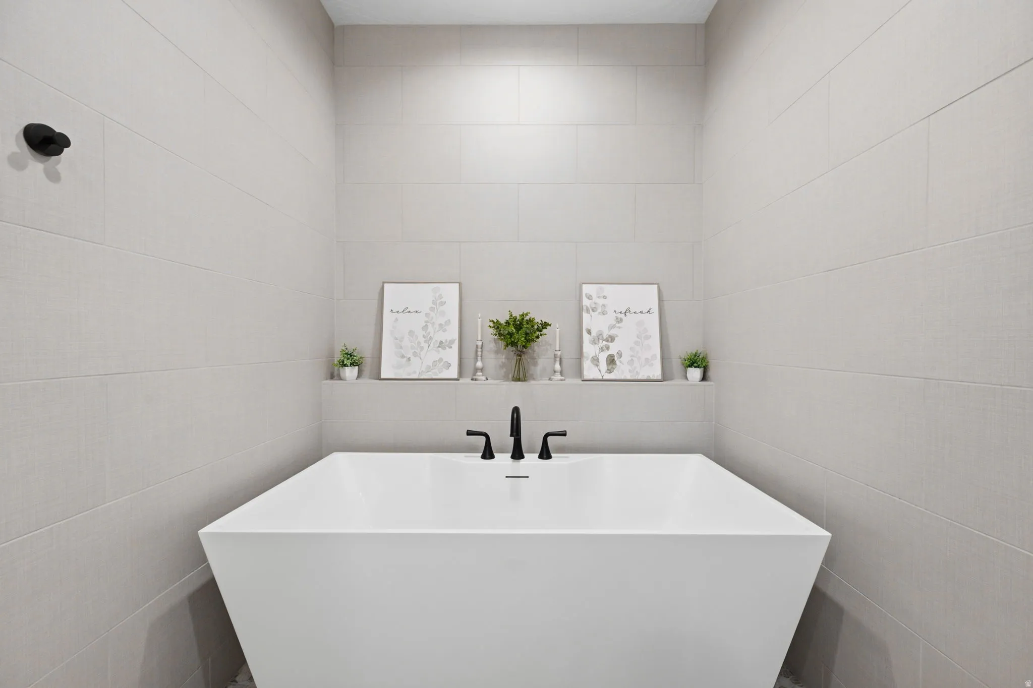 Freestanding soaking tub with matte black fixtures, integrated shelving, and full-height tiled walls