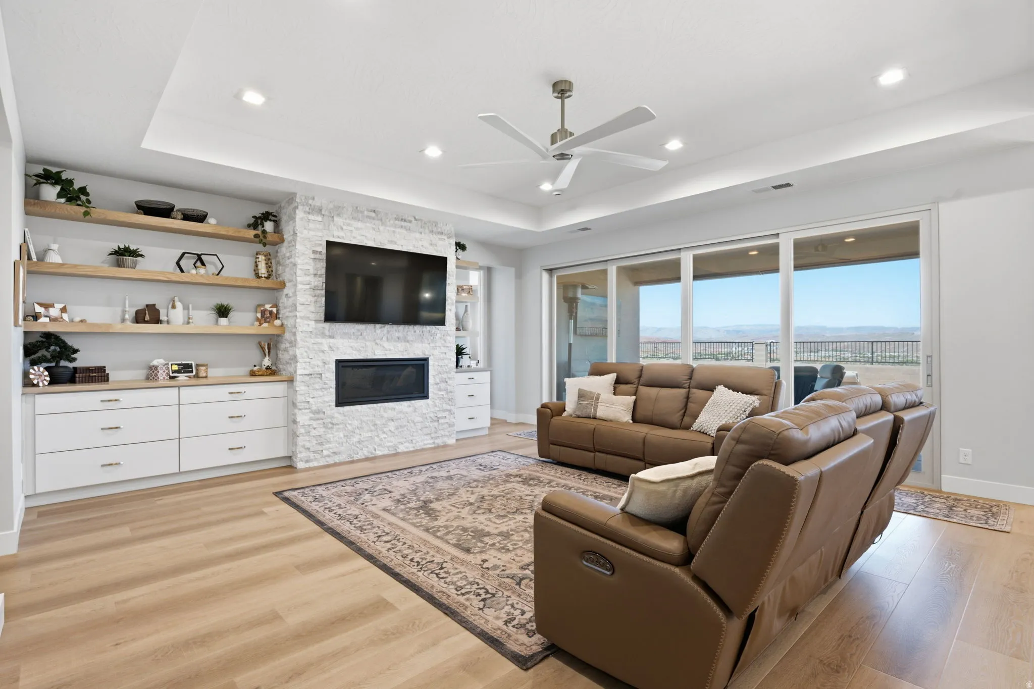 Spacious living area featuring LVP wood-finish flooring, a stone-clad fireplace, and built-in shelving with lower cabinetry