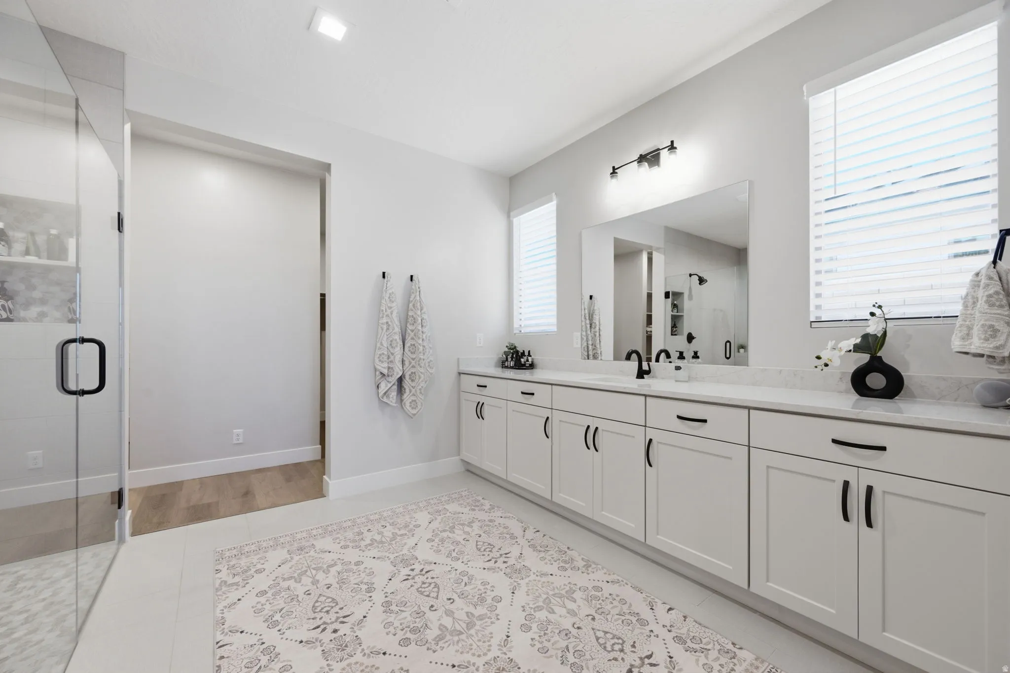 Spacious bathroom featuring a frameless glass shower enclosure, a vanity with white cabinetry, and a large mirror