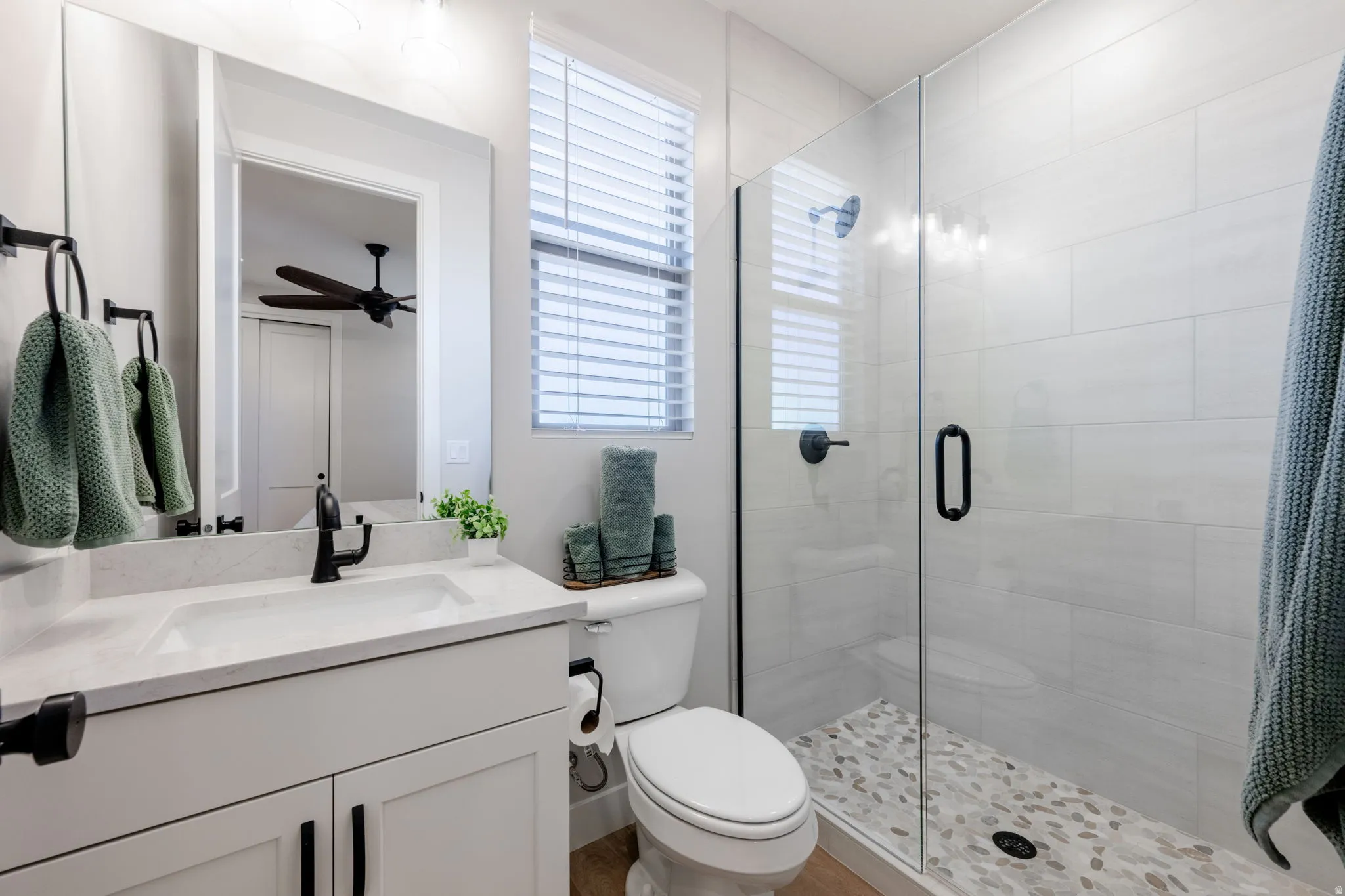Vanity with integrated sink and matte black faucet, glass-enclosed shower with pebble-finish flooring, and tiled walls