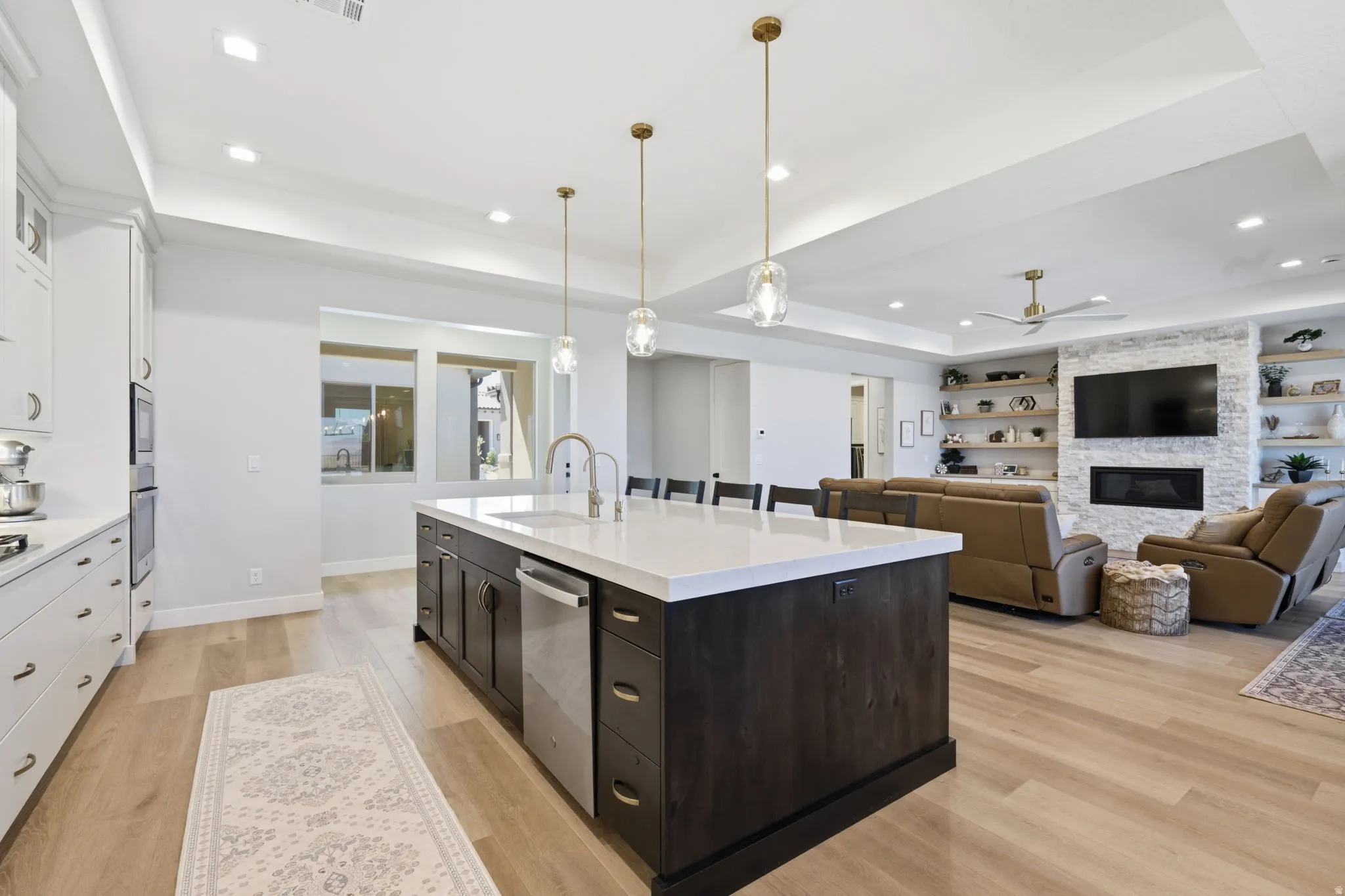 Open-concept kitchen and living area featuring LVP wood-finish flooring, a large kitchen island with a white countertop, and a living space with a fireplace and built-in shelving